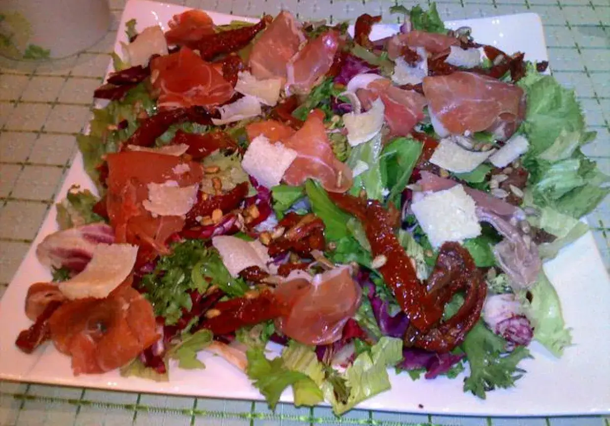 Pyszna sałatka z szynką parmeńską, suszonymi pomidorami i parmezanem, podana na białym talerzu.
