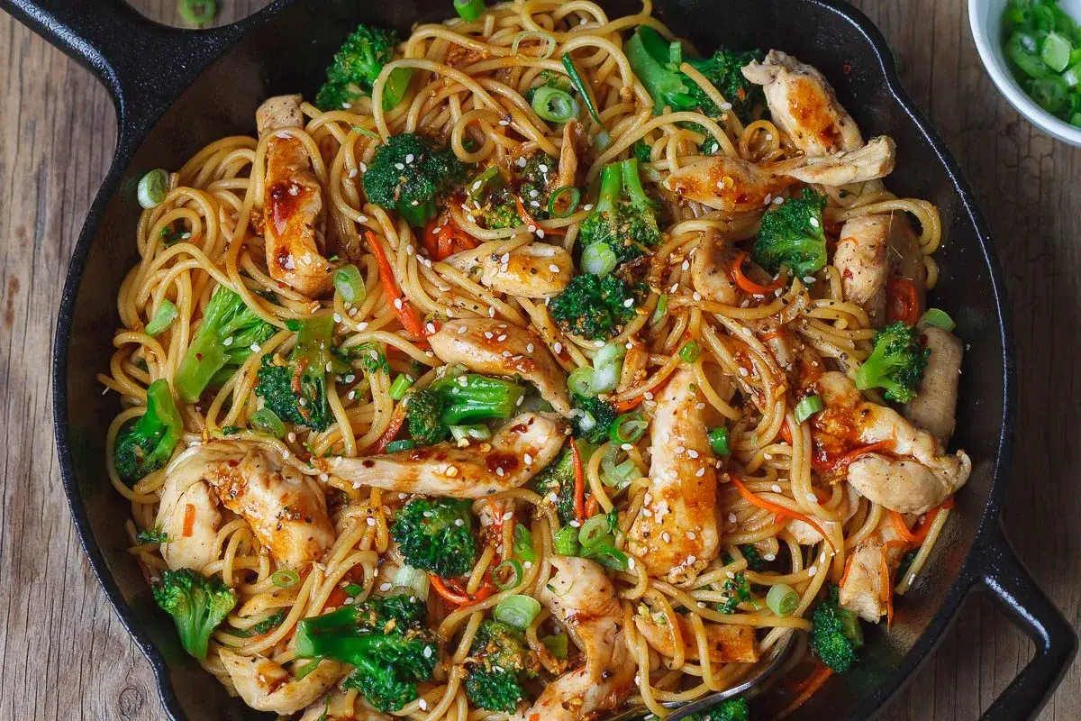 Pyszny makaron chow mein z kurczakiem, brokułami i marchewką, posypany sezamem.