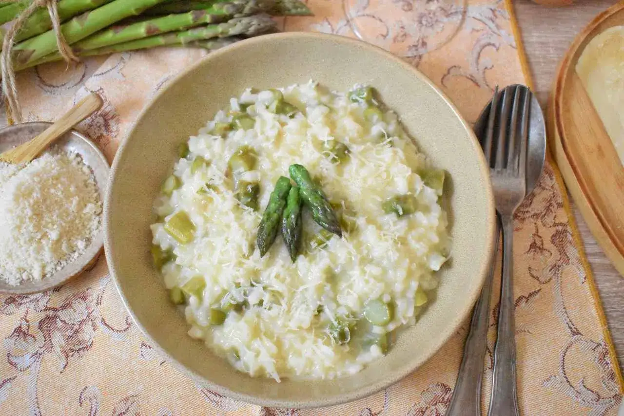 Kremowe risotto ze szparagami, posypane parmezanem, z trzema młodymi pędami szparag&oacute;w na wierzchu.