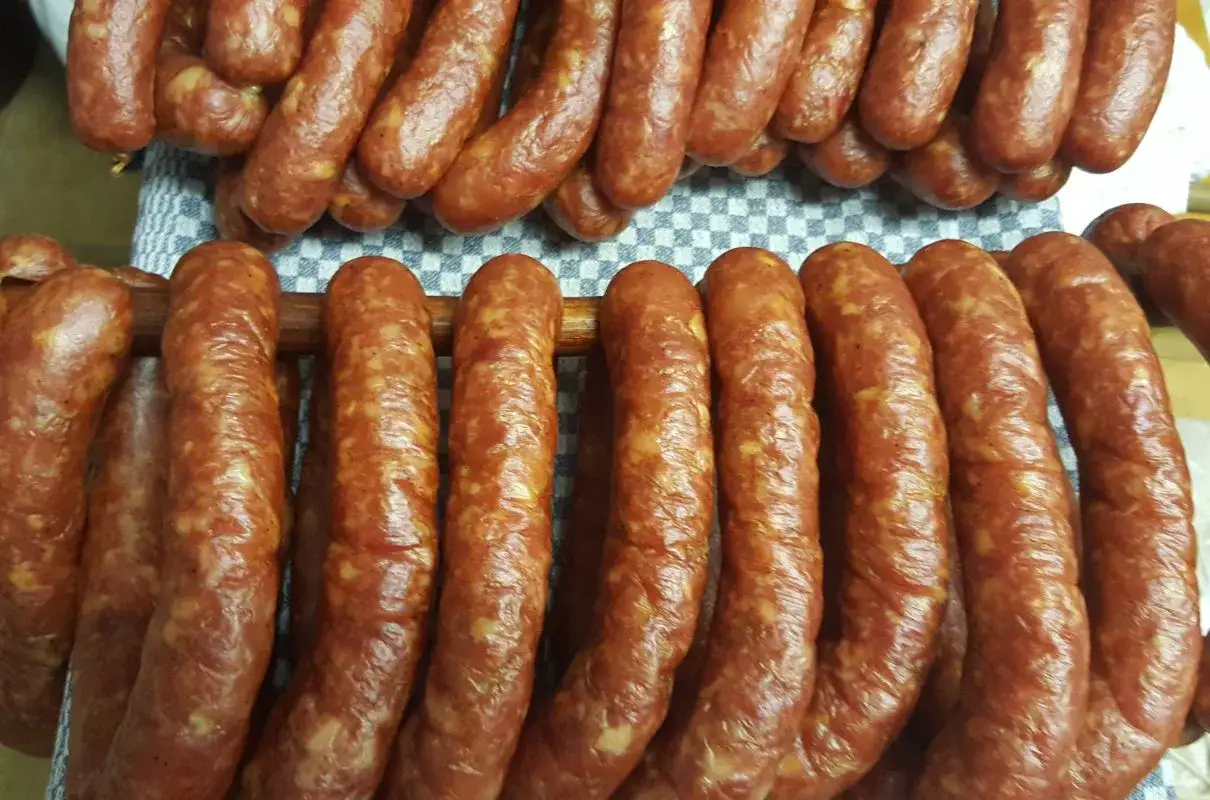 Prawdziwa wiejska kiełbasa przepis. Wędzone, domowe kiełbaski wiszą na drewnianych kijach, gotowe do dalszej obróbki.