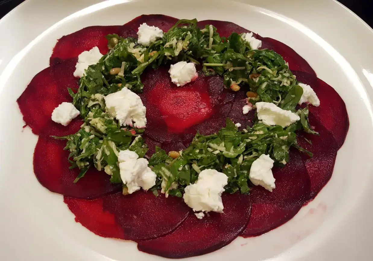 Carpaccio z buraka z rukolą, orzechami pinii i serem feta. Kolorowe plastry buraka tworzą bazę dla świeżej sałatki.