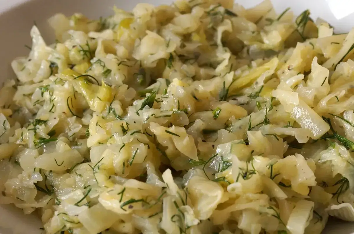 Młoda kapusta zasmażana z koperkiem, podana w białej misce. Aromatyczne danie, kt&oacute;re smakuje jak u babci.