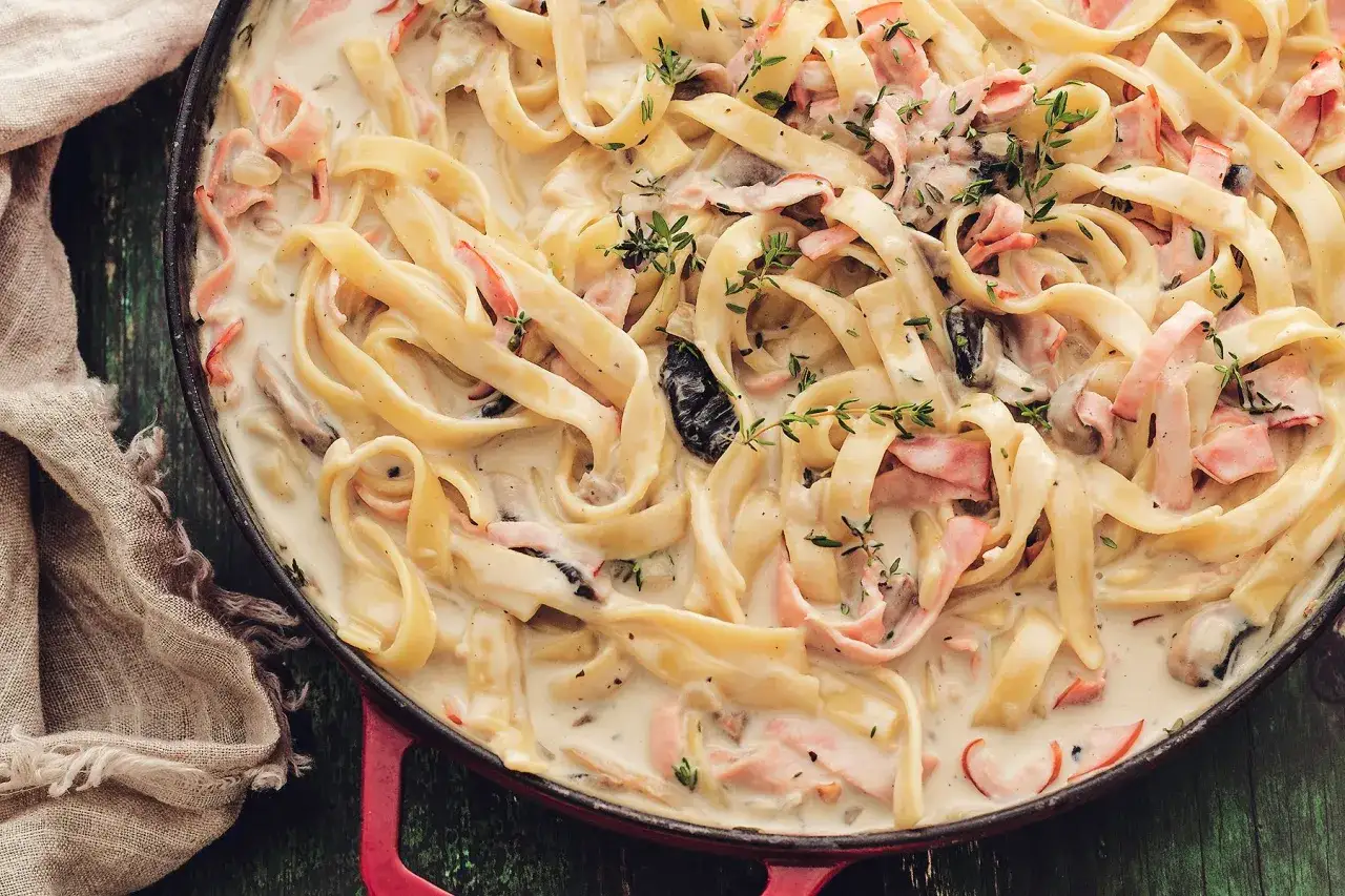 Tagliatelle w kremowym sosie z szynką i grzybami, pachnące jak najlepszy mac and cheese.