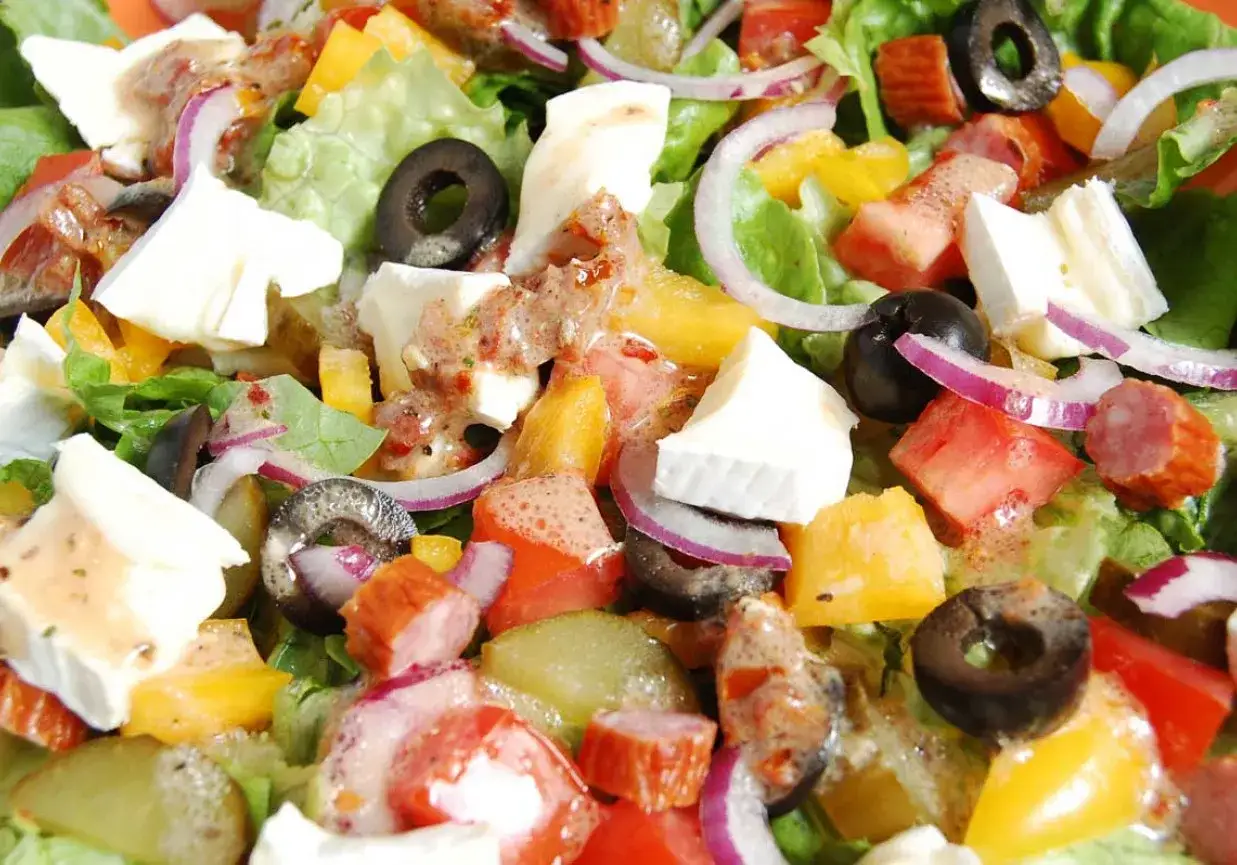 Kolorowa sałatka z kabanosem, serem feta, oliwkami, pomidorami, papryką i czerwoną cebulą, polana sosem.