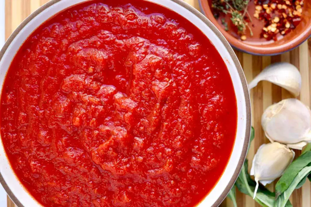 Gęsty, domowy sos do pizzy w misce, obok czosnek, zioła i płatki chili. Idealny na każdą okazję.