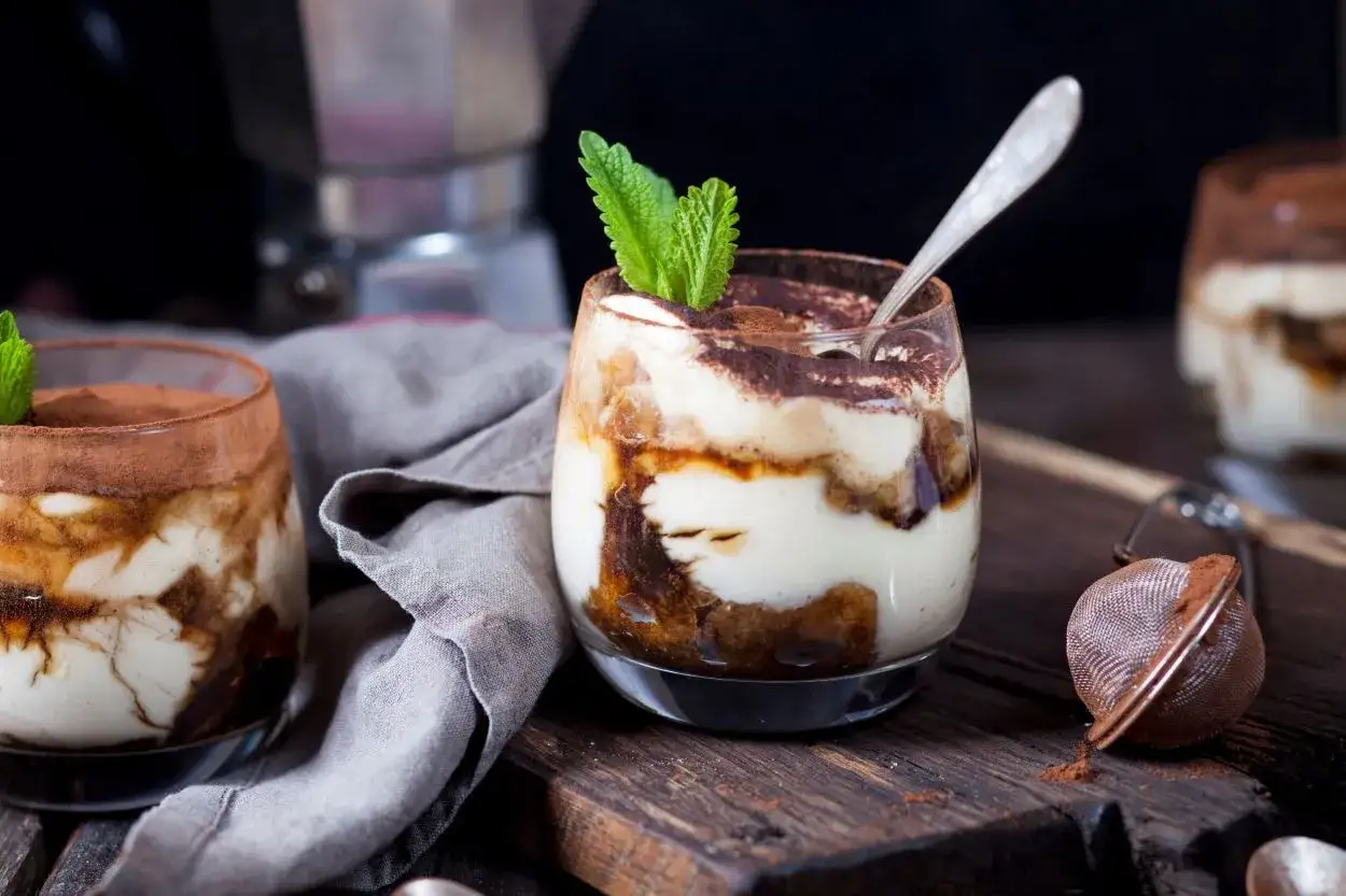 Pyszne tiramisu w pucharkach, udekorowane listkiem mięty i posypane kakao. Idealny deser na każdą okazję.
