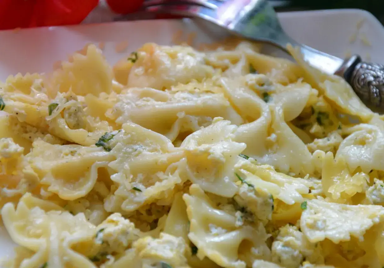 Pyszny makaron farfalle z jajkiem i serem, posypany zieloną pietruszką. Idealny na szybki obiad.