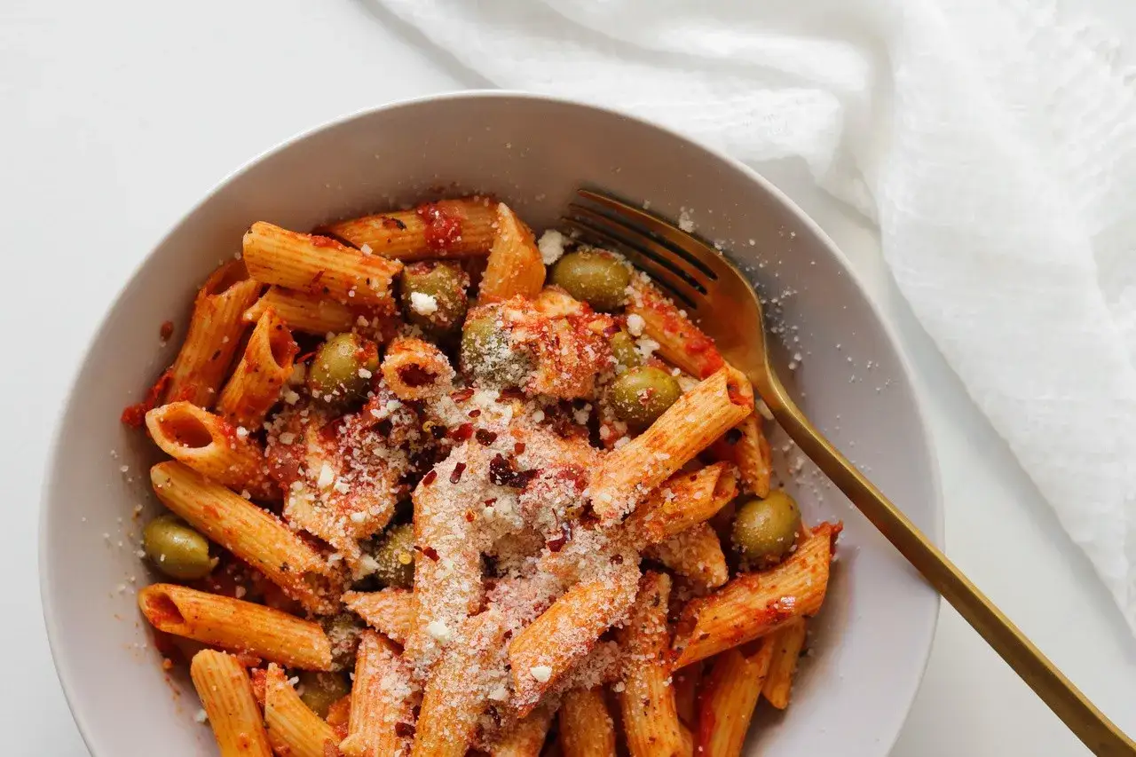 Szybki obiad z makaronem penne w sosie pomidorowym z oliwkami i parmezanem, gotowy w mgnieniu oka.