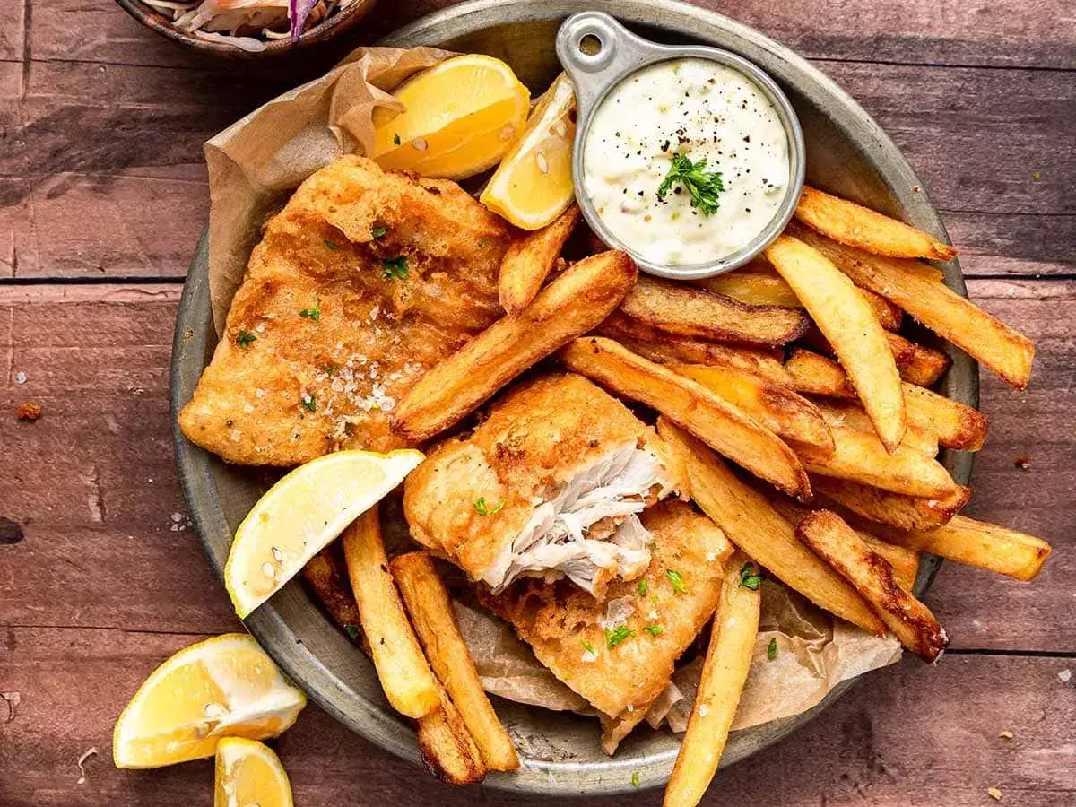 Chrupiące fish and chips z cytryną i sosem tatarskim, podane na talerzu.