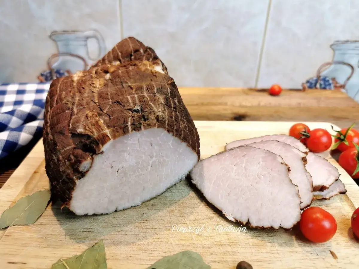 Aromatyczna szynka gotowana w herbacie, pokrojona w plastry, z pomidorkami koktajlowymi i liśćmi laurowymi na desce.