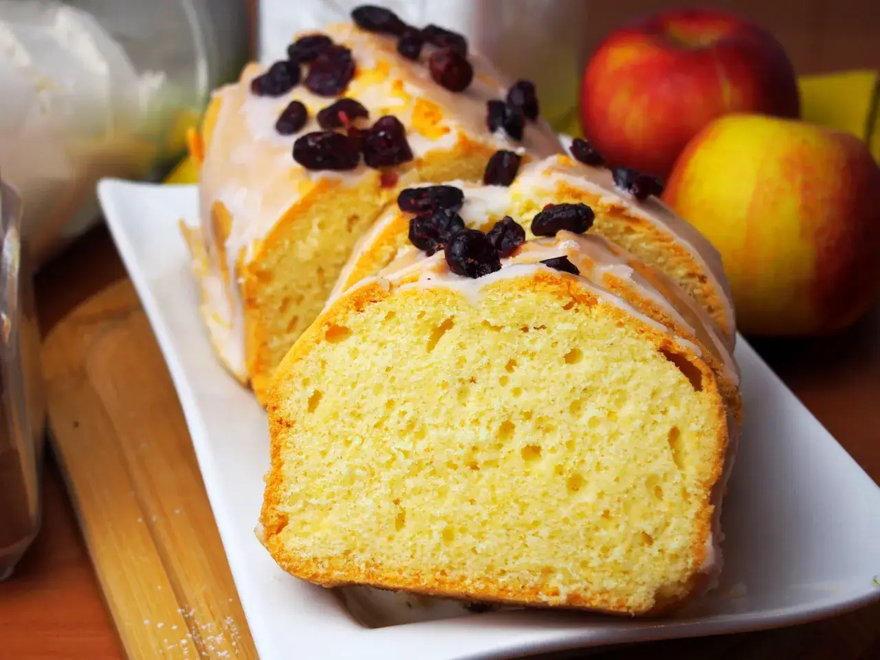 Pyszna babka piaskowa Ani gotuje, udekorowana lukrem i suszoną żurawiną, obok jabłek.