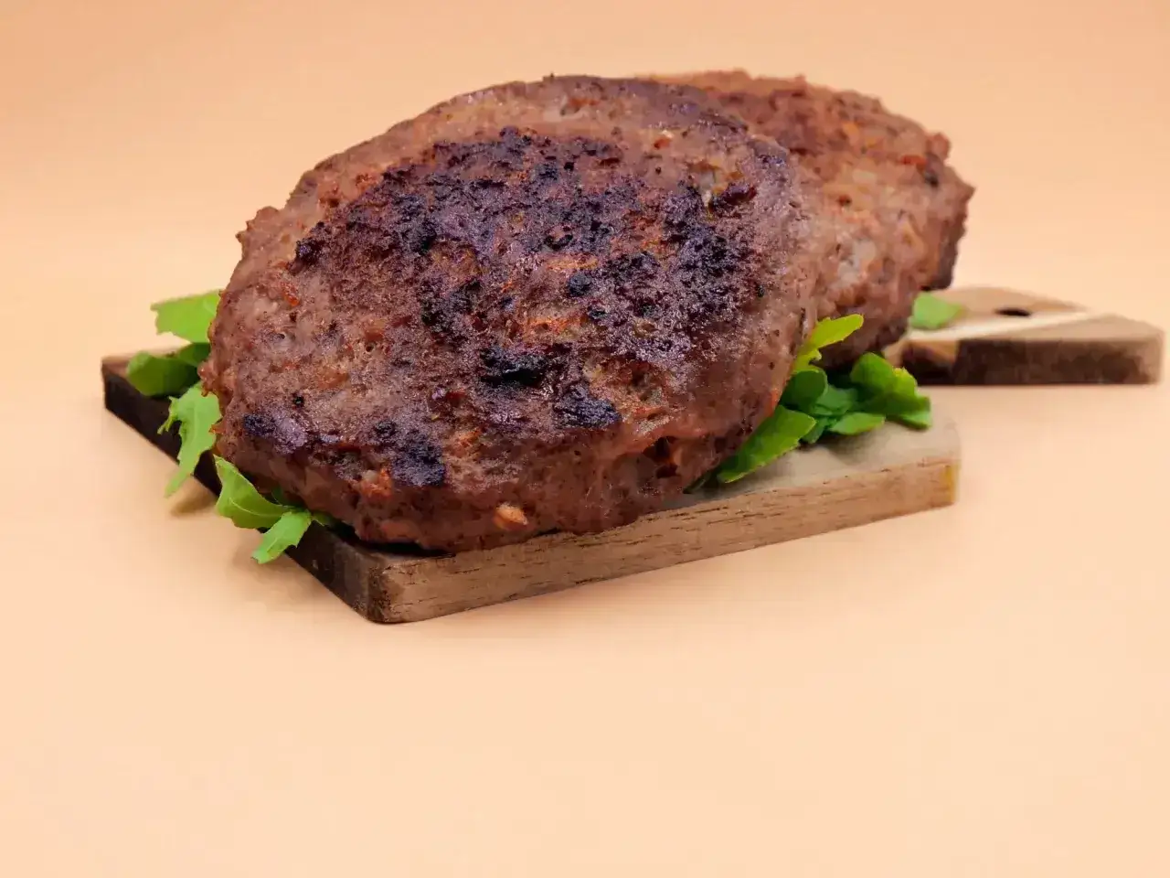 Dwa soczyste, grillowane mięso na burgery, ułożone na desce z rukolą, gotowe do skomponowania idealnego burgera.