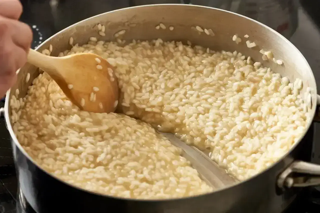Drewniana łyżka miesza kremowy ryż do risotto w garnku.