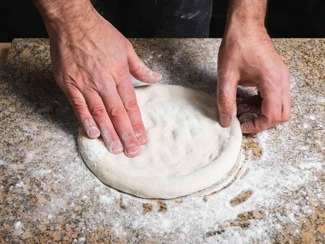 Dłonie formują okrągły placek na blacie. To będzie pyszna pizza bez drożdży.