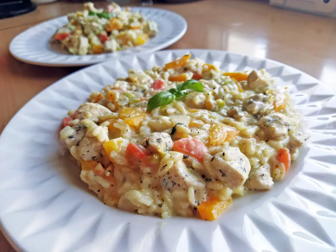 Pyszne risotto z warzywami i kurczakiem, udekorowane listkiem bazylii. Danie prezentuje się apetycznie na białym talerzu.