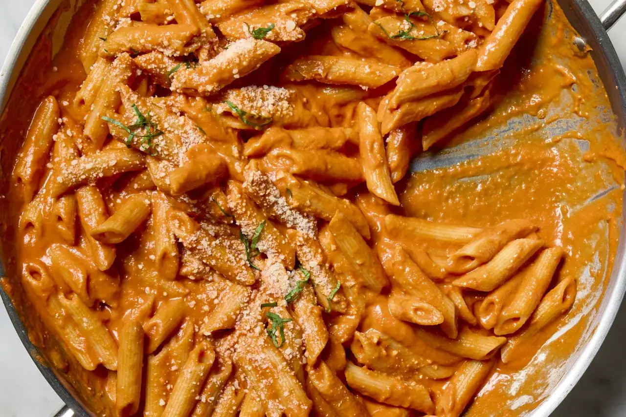 Penne alla vodka w kremowym, pomarańczowym sosie, posypane parmezanem i świeżą bazylią, gotowe do podania.